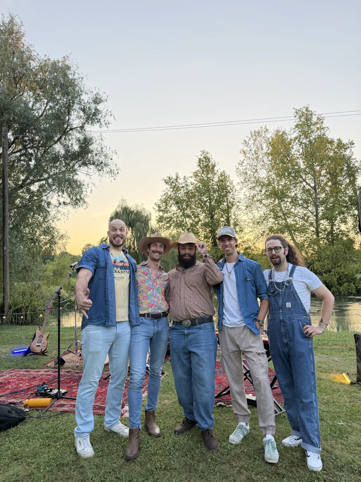 The five musicians of Hot Joe & The Coffeekillers posing by the river at sunset, their instruments resting on the ground