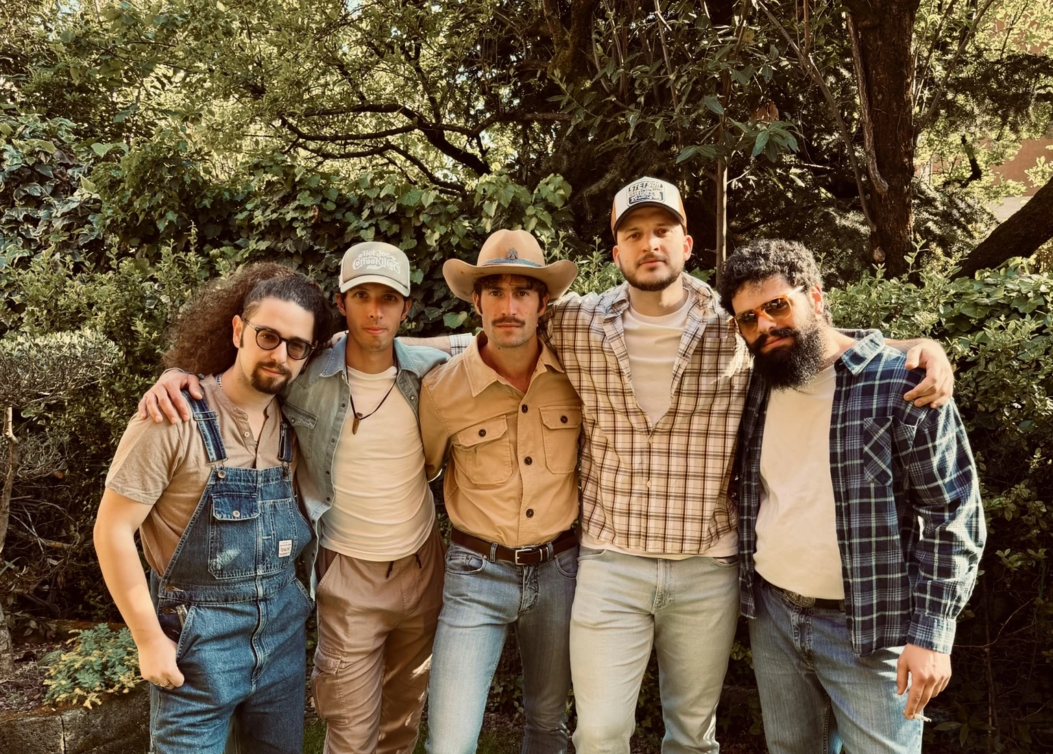 Hot Joe & The Coffeekillers, i cinque musicisti della band country di Brescia abbracciati in giardino, tra cappelli da cowboy, camicie a quadri e salopette