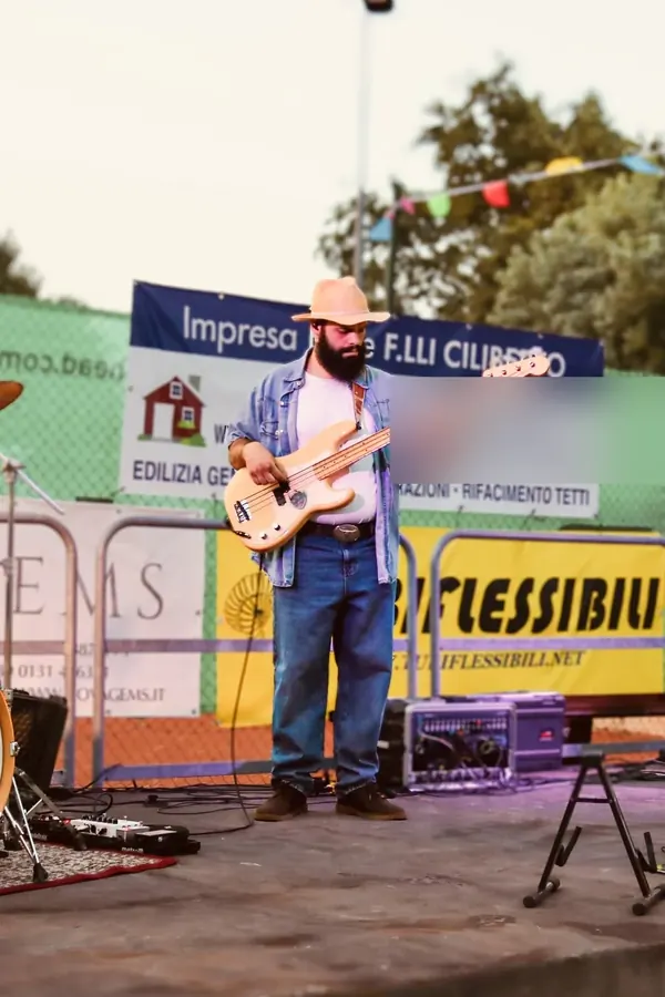 Richi on bass, hat on, on stage at a village fair