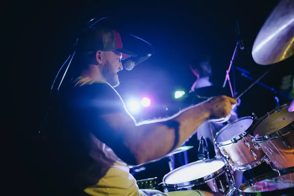 Miglio in profile behind the cymbals, in blue and purple stage light