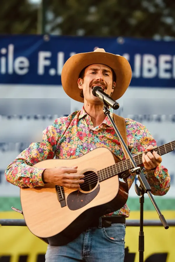 Mike singing with his acoustic guitar, country hat and flowered shirt, during a show