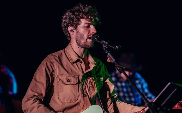 Mike canta al microfono con giacca beige durante un concerto serale