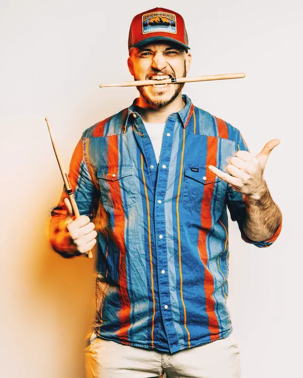 Studio portrait of Miglio in a striped shirt, a drumstick between his teeth