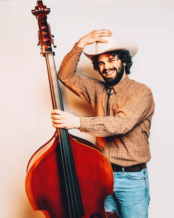 Studio portrait of Richi in a country hat, hugging his double bass