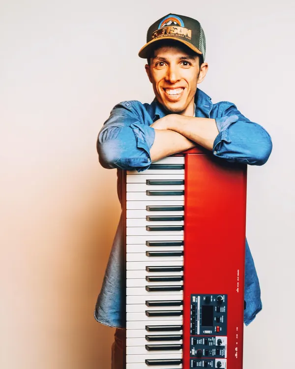 Studio portrait of Larry leaning on his red Nord keyboard