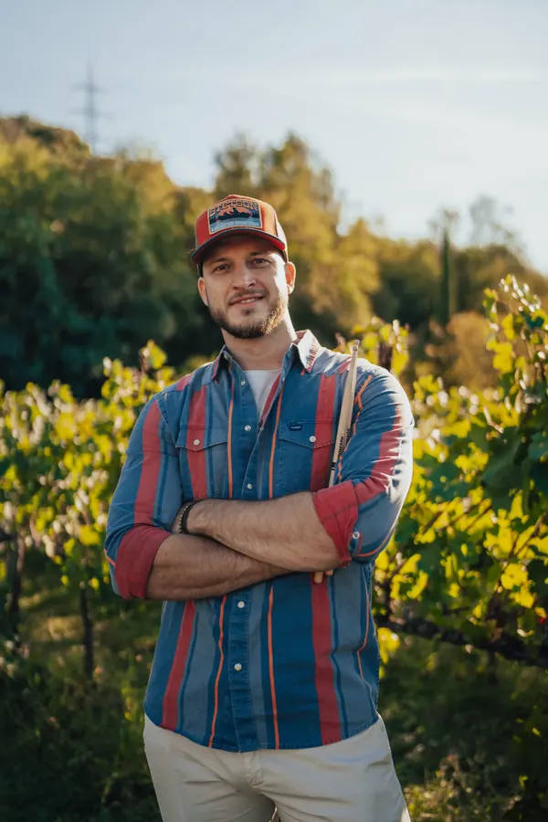 Portrait of Miglio among the vines, cap and striped shirt, arms folded