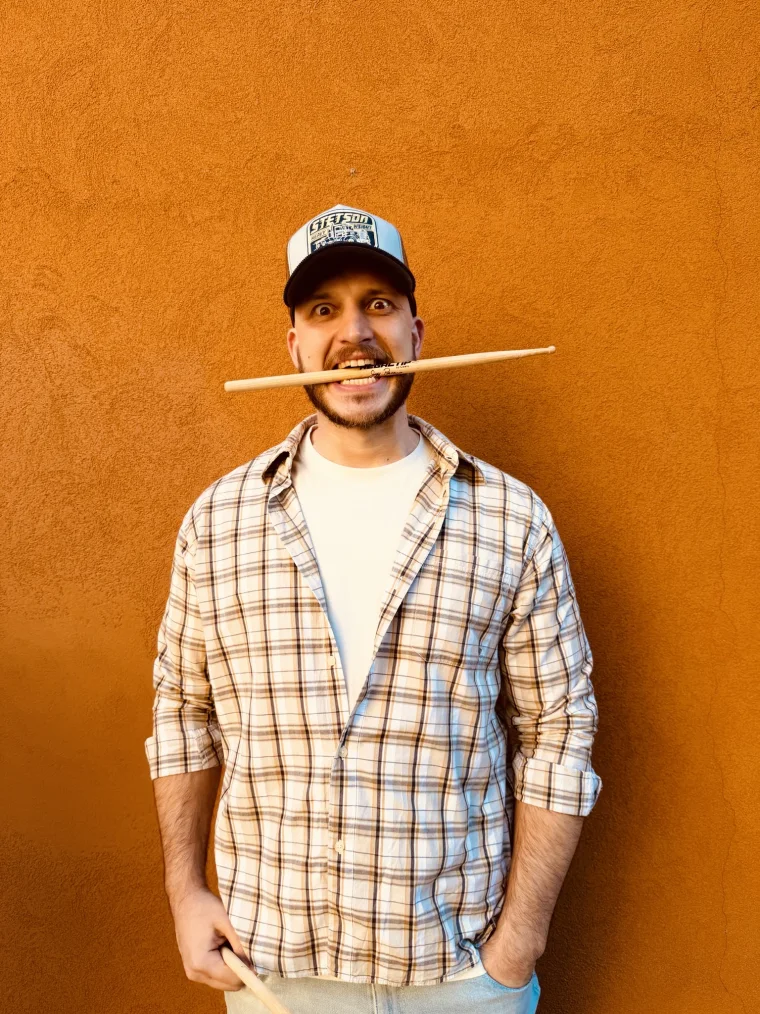 Davide &ldquo;Miglio&rdquo; Miglietti con le bacchette in bocca, davanti a un muro arancio