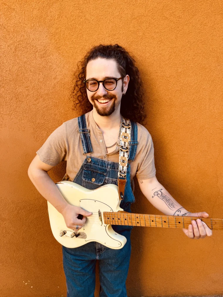 Stefano &ldquo;Ste&rdquo; Martinelli con la Telecaster bianca e la salopette, davanti a un muro arancio